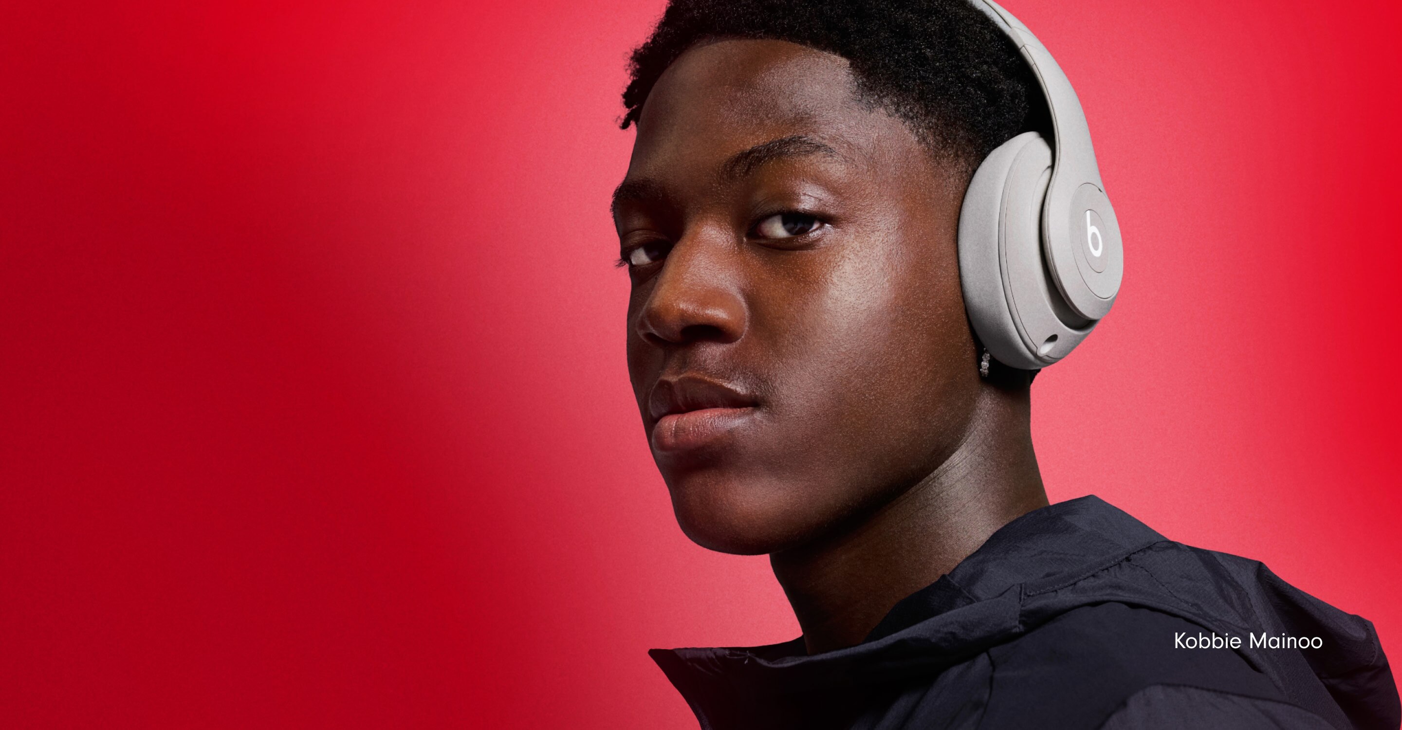 Footballer Kobbie Mainoo wearing Beats Studio Pro headphones in Sandstone against a red background, with the text "Flip Their Script."