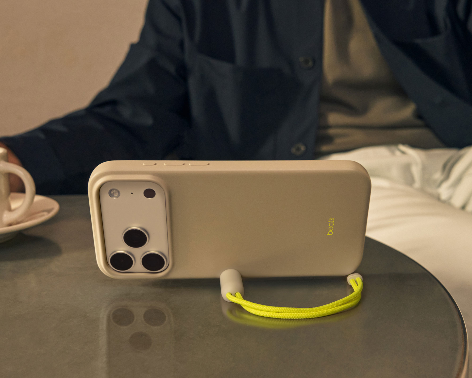The Beats iPhone 17 Kickstand Case with MagSafe and Camera Control in Lime Stone shown propped up to demonstrate the lanyard kickstand in action.