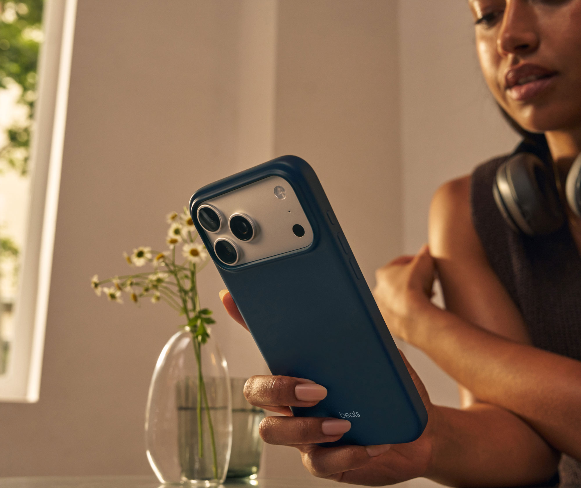 A woman holding the Beats iPhone 17 Case with MagSafe and Camera Control in Pebble Pink featuring an outer matte finish.