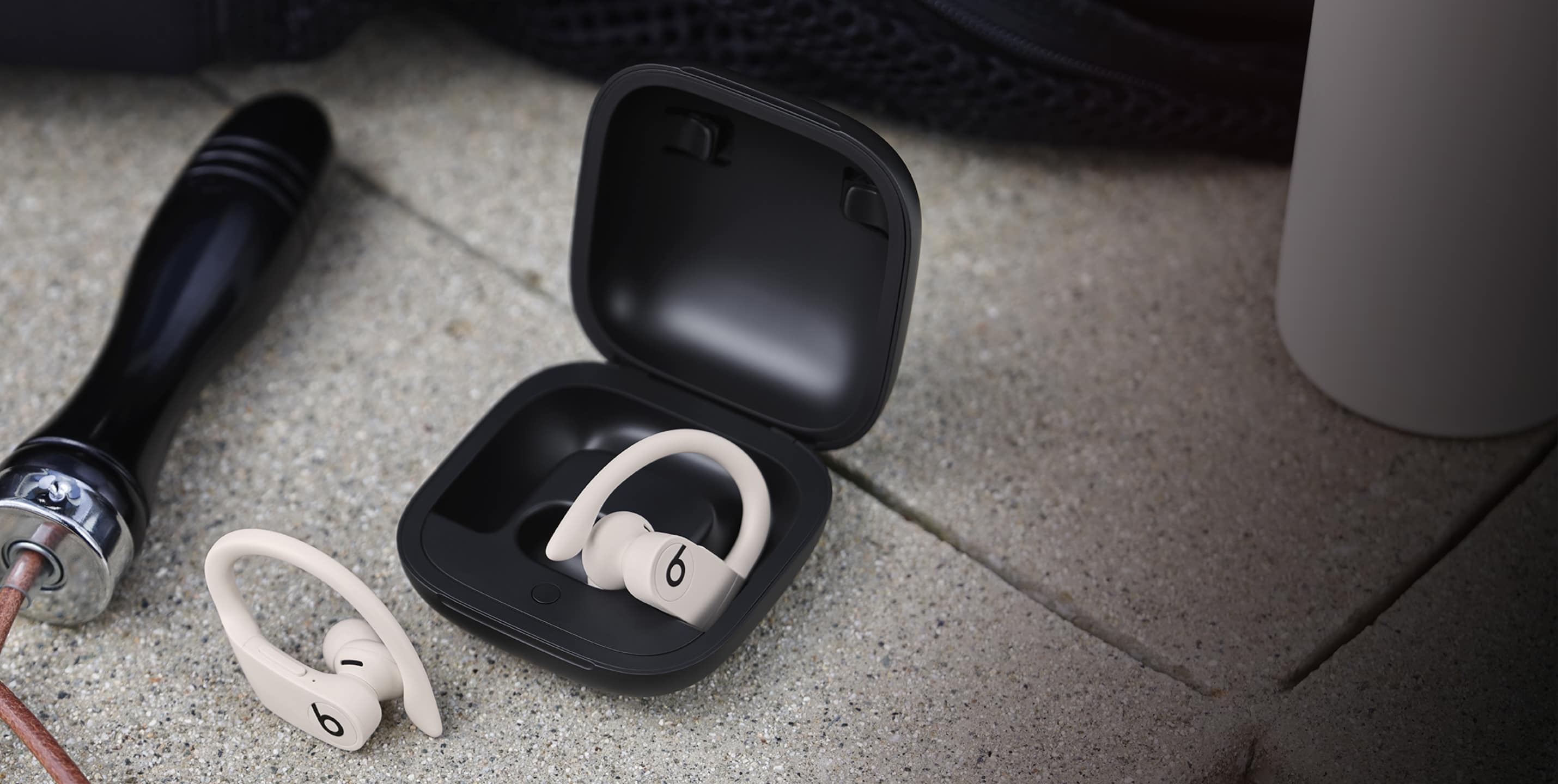 象牙白 Powerbeats Pro 带有黑色充电盒,旁边是在水泥地上的跳绳。