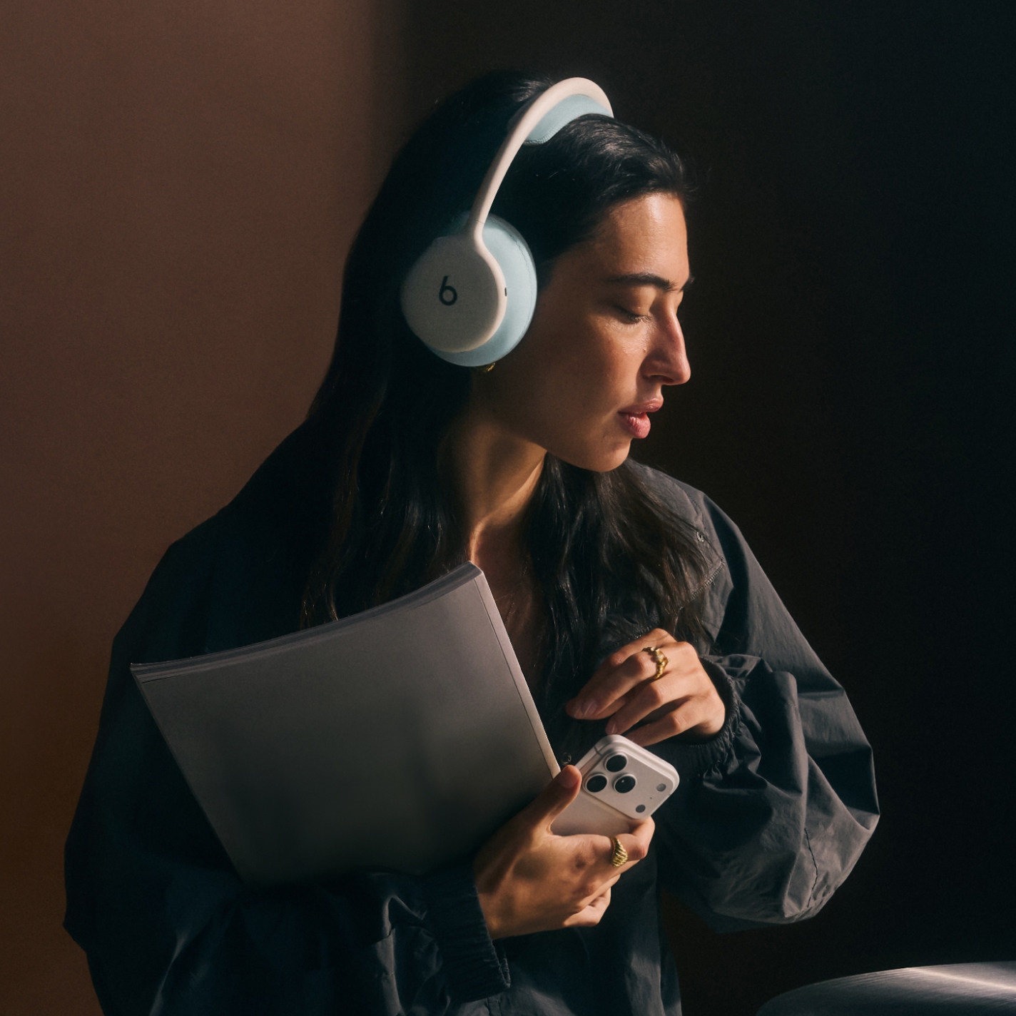 一人戴着 Beats 360 头戴式耳机并手持 iPhone，展示出色的通话质量和主动降噪功能