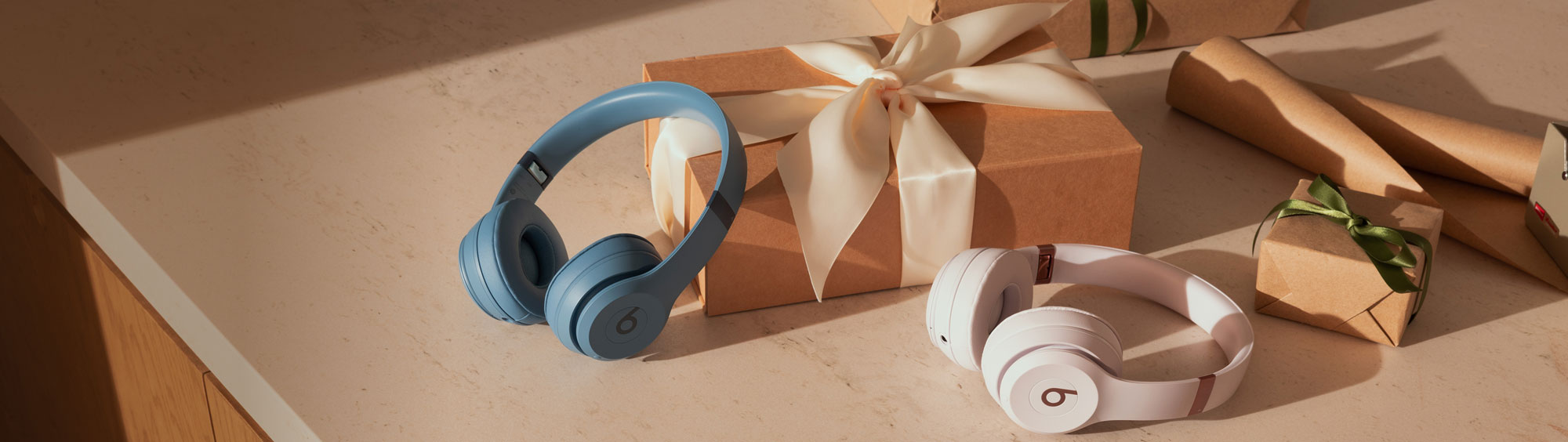 Beats Studio Pro and Beats Solo 4 with wrapped gifts behind them on top of a counter.