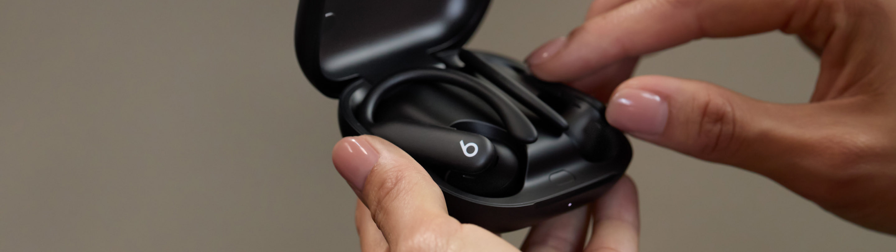 A pair of black Powerbeats Pro 2 earbuds are held inside their open charging case by hands.